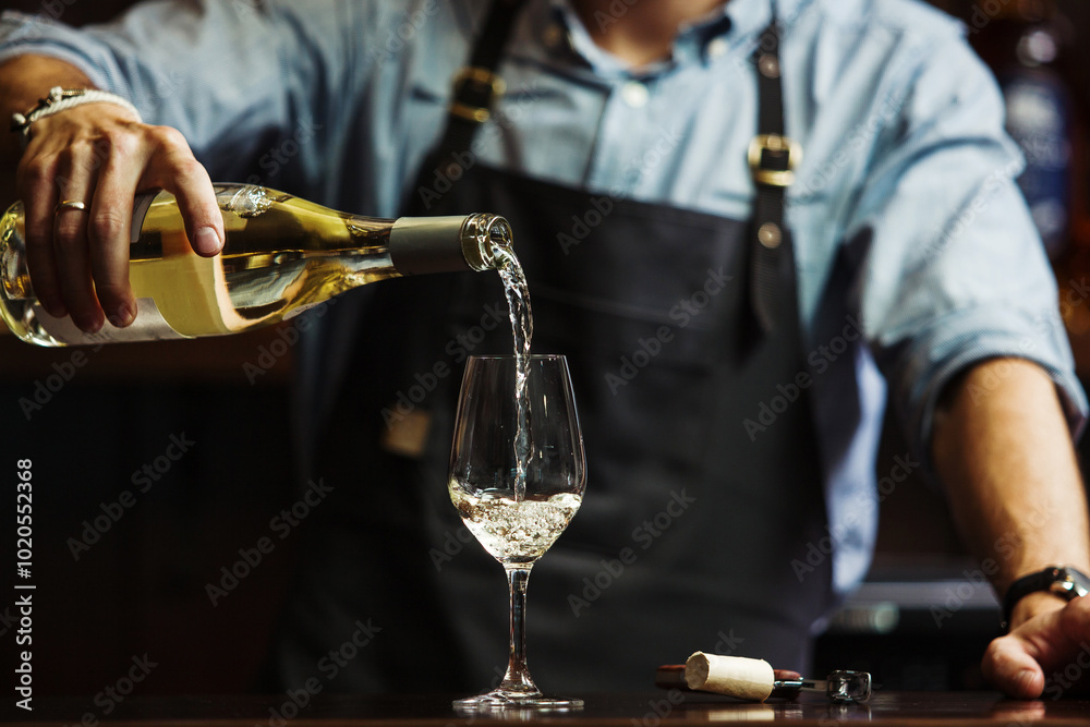 Fototapeta premium Male sommelier pouring white wine into long-stemmed wineglasses.