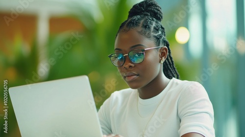 A young woman is intently studying with a laptop and notebook in a bright cafГ©, surrounded by greenery and natural light