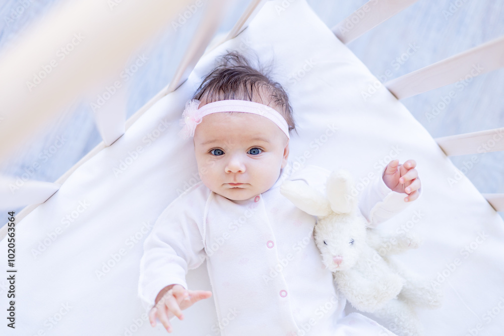 portrait of a baby girl smiling on a bed on a white cotton bed with a toy falling asleep or waking up in the morning, a cute newborn baby at home in a crib close-up portrait of a baby girl smiling on a bed on a white cotton bed with a toy falling asleep or waking up in the morning, a cute newborn baby at home in a crib close-up