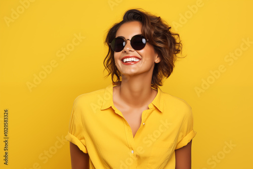 Smiling woman in sunglasses and yellow shirt against yellow background