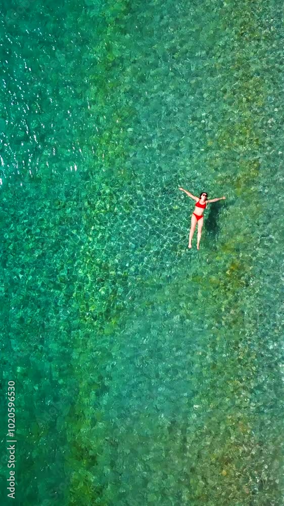 Woman in red swimsuit floats in the clear sea, top down view Woman in red swimsuit floats in the clear sea, top down view