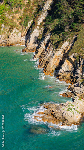 View of a rocky cliff contrasting with the turquoise water and green vegetation on a sunny day, perfect for going to the beach photo