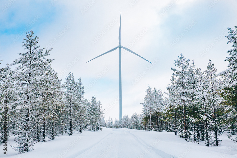 Wind turbines in winter landscape with snow covered trees and snow road in Finland, Europe. Alternative energy in winter. Wind turbines in winter landscape with snow covered trees and snow road in Finland, Europe. Alternative energy in winter.