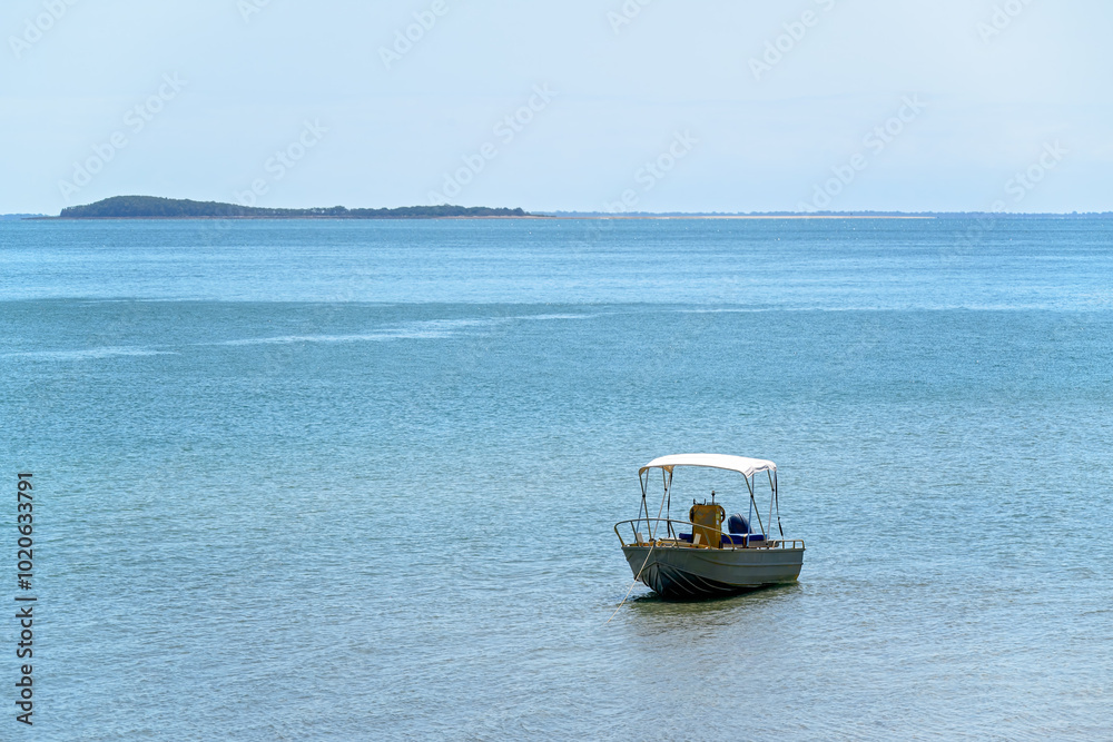 Obraz premium Boat dinghy on calm ocean water, blue cloudless sky, sunny day