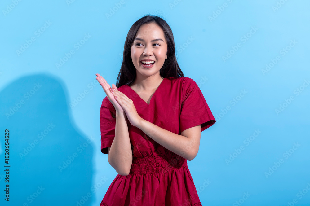 Asian woman wearing a red dress claps her hands in excitement while looking off to the side. She appears joyful and expressive against a light blue background, conveying positive energy and enthusiasm Asian woman wearing a red dress claps her hands in excitement while looking off to the side. She appears joyful and expressive against a light blue background, conveying positive energy and enthusiasm