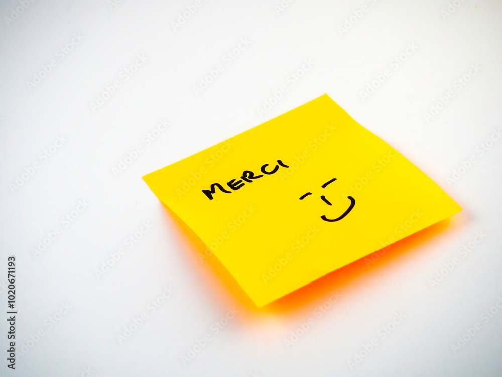 Yellow sticky note with Merci written on it, French for thank you. On a light background Yellow sticky note with Merci written on it, French for thank you. On a light background