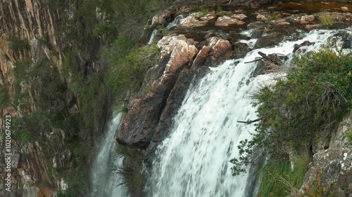 Slow-motion shot from the top of Minyon Falls, capturing water gracefully cascading down the rocky ledge, surrounded by lush greenery and natural beauty. photo