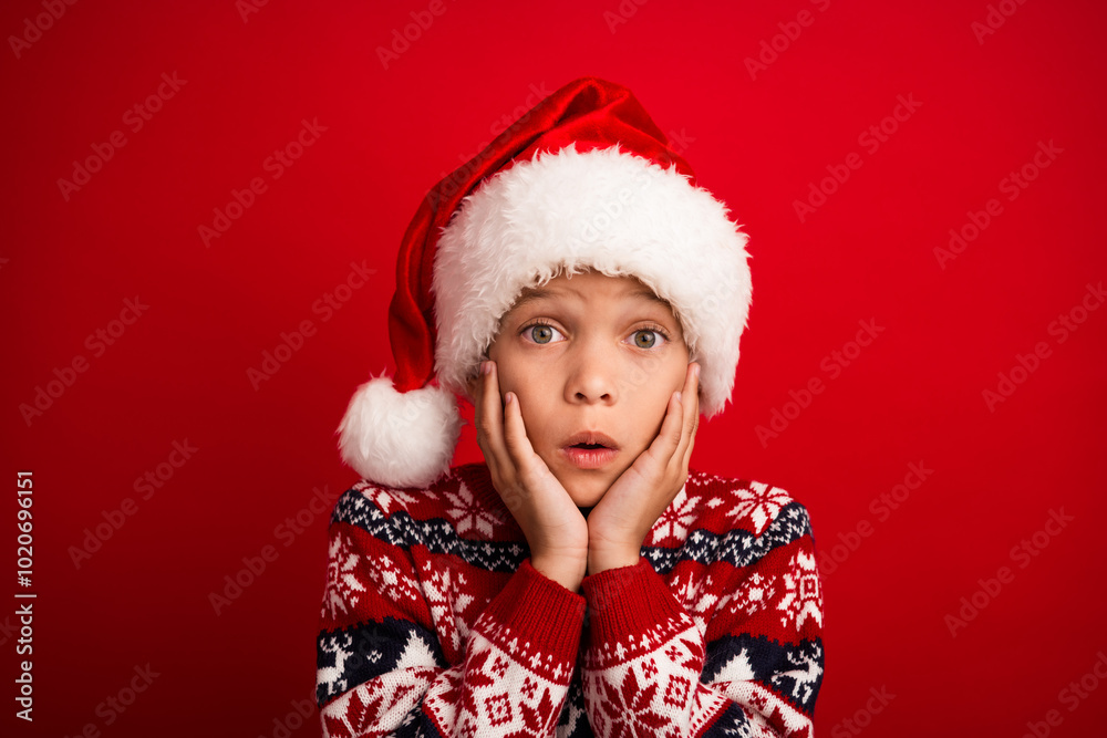 Photo portrait of cute little boy shocked reaction touch cheeks celebrate christmas wear knitwear sweater isolated on red color background Photo portrait of cute little boy shocked reaction touch cheeks celebrate christmas wear knitwear sweater isolated on red color background