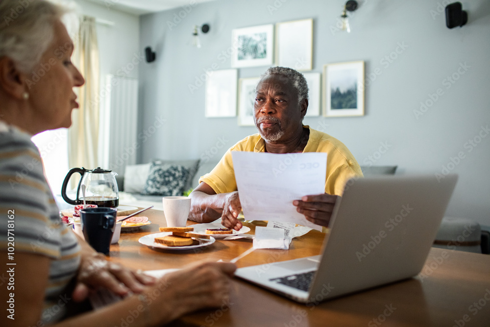 Diverse senior couple going over financials with laptop during breakfast Diverse senior couple going over financials with laptop during breakfast