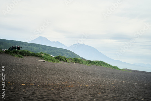 Khalaktyrsky Beach, Kamchatka. A tranquil coastal scene showcases black sand, gentle waves, and beautiful lush green hills set in the backdrop photo