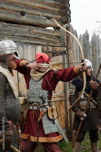 Three individuals dressed in medieval attire engaging in archery event with rustic wooden backdrop capturing historical ambiance