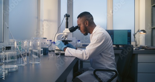 Medical science laboratory: African American biochemist looks under microscope, does analysis of test sample, develops drugs. Professional scientist uses high-tech equipment. Pharmacology. Dolly Shot.