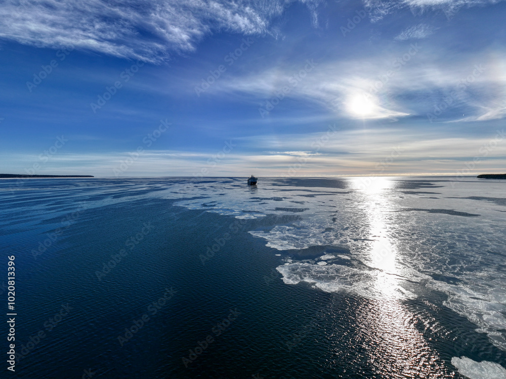 Cargo Ship Far Away in the Horizon on a Bright, Sunny, Clear Winter Day on a Calm, Dark Blue Semi-Frozen Sea