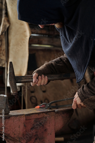 Slika na platnu Person hammering heated metal on anvil in dimly lit workshop, wearing protective