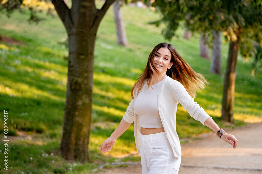 Young woman is spinning around with open arms, enjoying a sunny day in the park Young woman is spinning around with open arms, enjoying a sunny day in the park