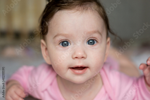 A small child or girl or baby or toddler or newborn lying on her stomach looking at the camera and smiling. Close-up portrait of a child. A baby with big blue eyes and dark hair