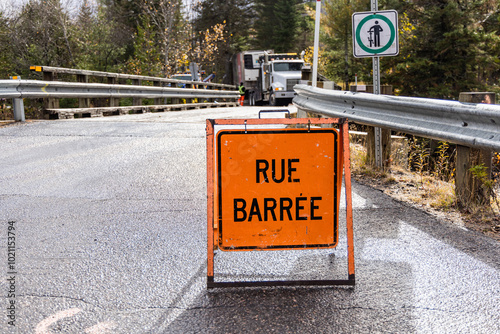 Orange road closed sign blocking access to a bridge while construction workers are busy working in the background. Selective focus