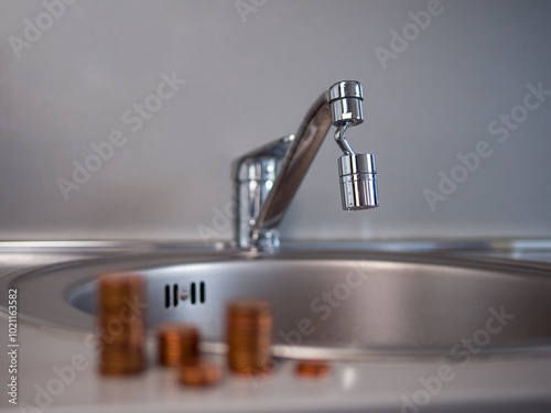 A faucet releases water in a consistent stream, while coins are arranged in neat columns in the foreground. The faucets flowing water contrasts beautifully with the stillness of the shining coins.