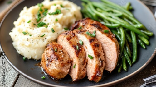 Sliced grilled chicken with creamy mashed potatoes and crisp green beans on a dark plate.