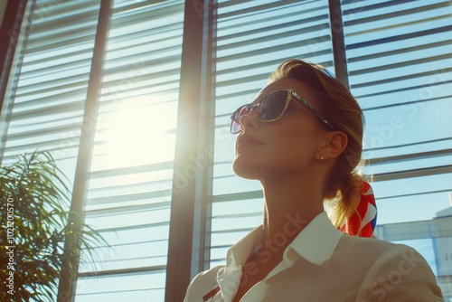 A woman wearing a white shirt and sunglasses looks out a window, potentially planning her day or contemplating something