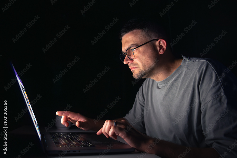 Young man works at the computer at night.