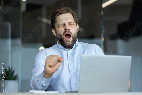 Tired office worker yawning in front of a laptop at work