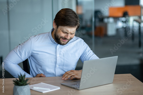 Stressed businessman experiencing back pain at his desk