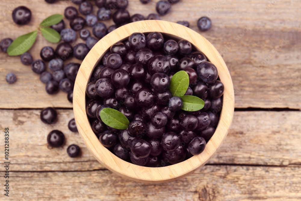 Ripe acai berries and leaves in bowl on wooden table, top view