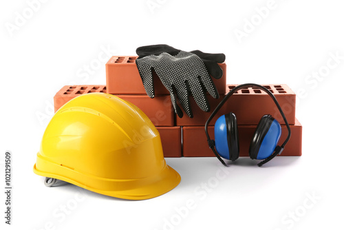 Yellow hard hat, red bricks, gloves and earmuffs isolated on white. Building material and safety equipment photo