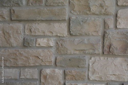 Close up of a square cut gray stone wall with elements of brown, yellow, orange, and cream earth tones on the front entrance of a home. photo