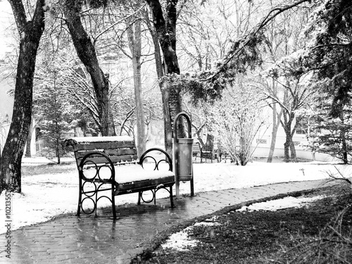 A bench in the park is under snow in winter. Black and White