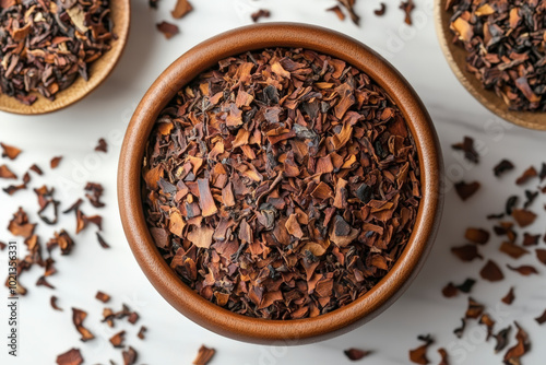 A wooden bowl filled with loose leaf roasted cacao nibs, surrounded by scattered nibs, creating a warm and rustic presentation on a light background.