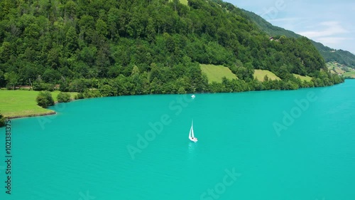Drone footage of turquoise clear lake Lungern or Lungerersee in Switzerland in summer sunny day with village and green meadow