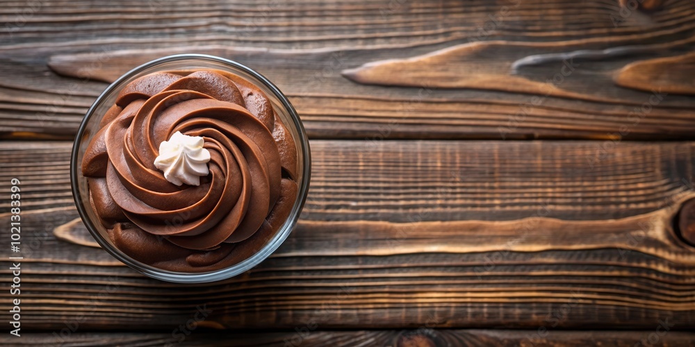 A swirl of rich chocolate mousse with a dollop of whipped cream in a glass dish sits on a rustic wooden background. A swirl of rich chocolate mousse with a dollop of whipped cream in a glass dish sits on a rustic wooden background.