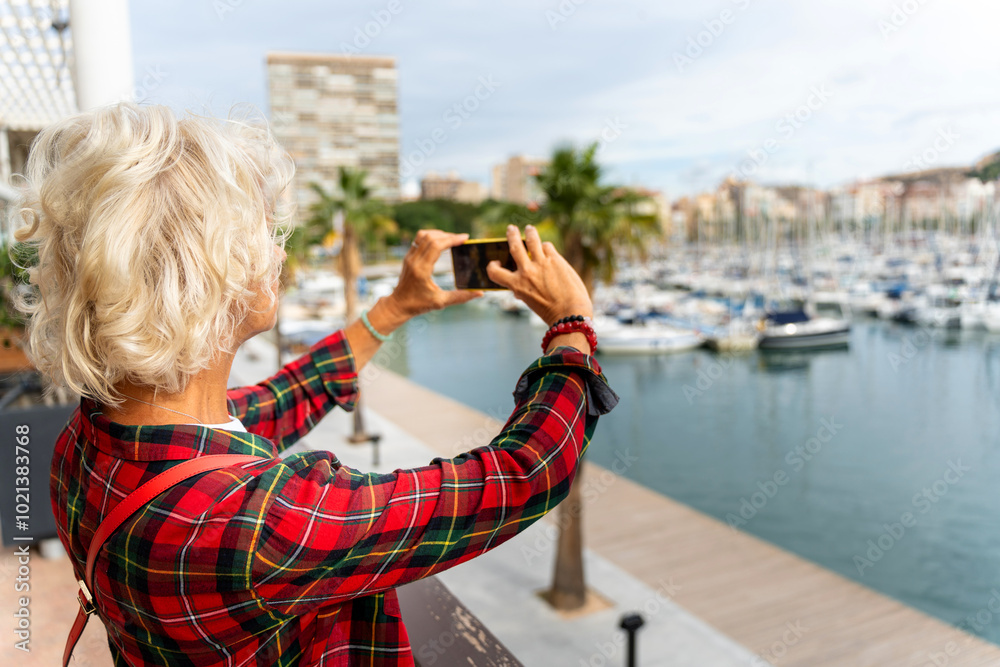 Female tourist over 60 taking a photo of the boats in the port with her mobile phone. Female tourist over 60 taking a photo of the boats in the port with her mobile phone.