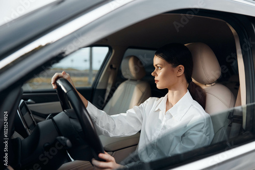 Woman driving car, hands on steering wheel, looks at camera, driver's seat, daytime