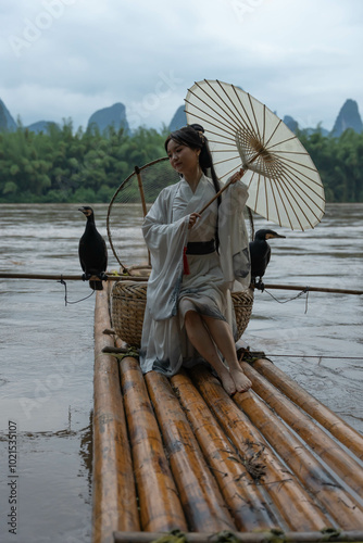 Hanfu girl with umbrella on bamboo raft in Xingping posing with cormorants