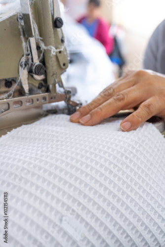 Manos expertas cosiendo tela blanca en una máquina overlock, Detalle de una operación de costura en una fábrica textil photo