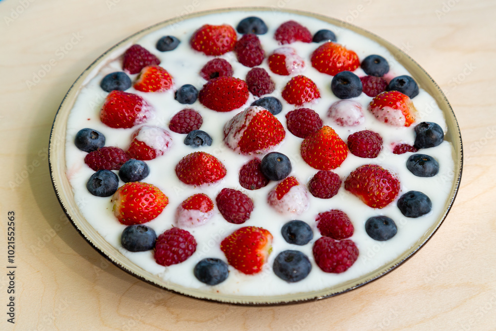 In a plate with whipped cream, strawberries, raspberries and blueberries on a gray table