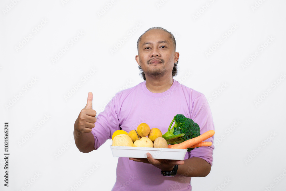 curly-haired Asian adult male carrying a tray of fresh vegetables while pointing at it, curly-haired Asian adult male carrying a tray of fresh vegetables while pointing at it,