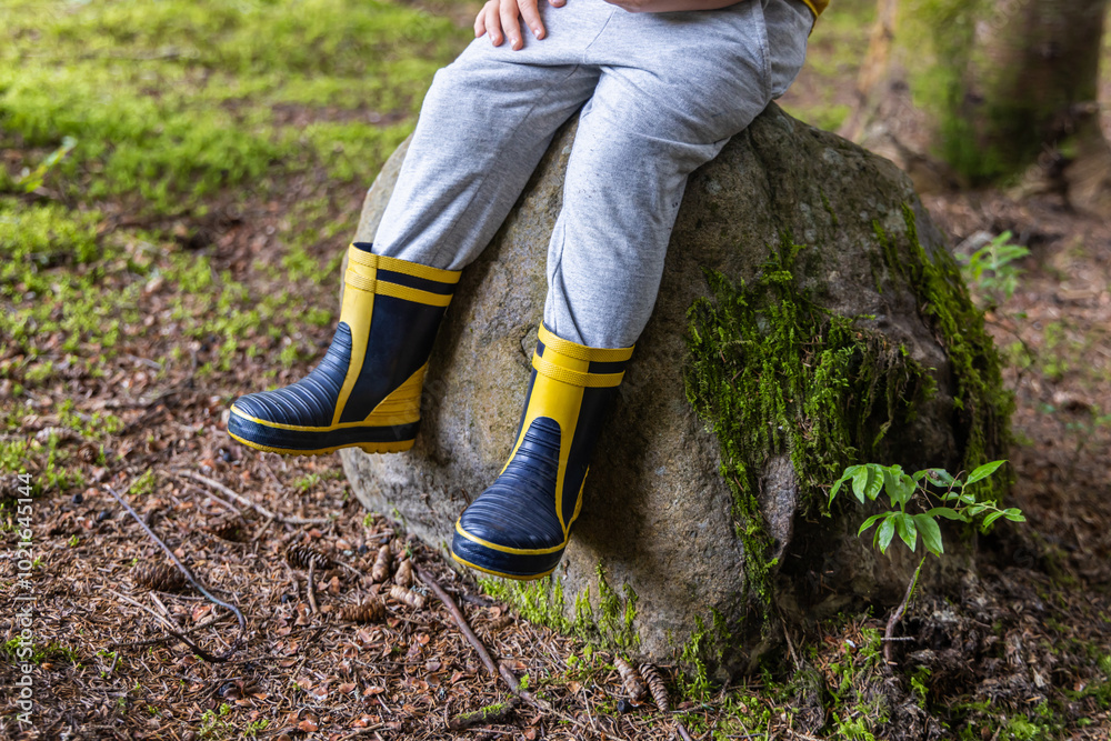 Boy is taking a break from exploring, sitting on a moss covered rock in the forest. Selective focus Boy is taking a break from exploring, sitting on a moss covered rock in the forest. Selective focus