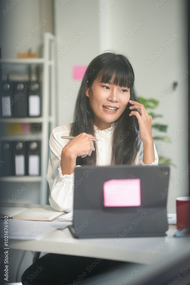 Businesswoman is smiling while talking on her phone and holding a pen in her office Businesswoman is smiling while talking on her phone and holding a pen in her office