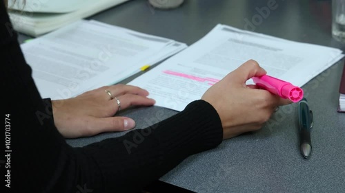 Woman highlights text on a document with a pink highlighter in slow motion, showcasing focus and concentration. Selective focus