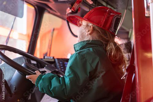 Young boy is sitting in the driver's seat of a firetruck wearing a firefighter's helmet and smiling. Selective focus