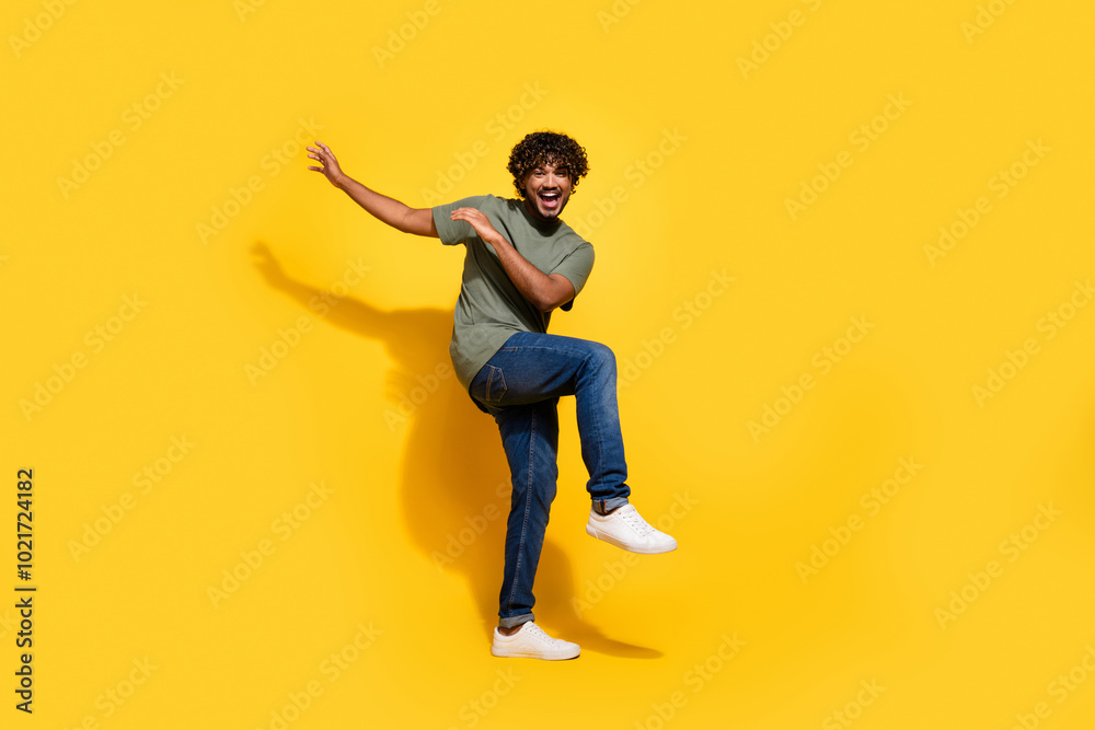 Full size photo of cheerful nice guy dressed khaki t-shirt jeans raising palms up dancing on party isolated on yellow color background Full size photo of cheerful nice guy dressed khaki t-shirt jeans raising palms up dancing on party isolated on yellow color background