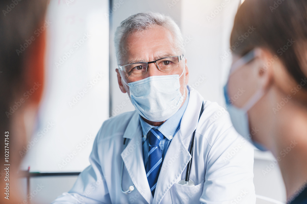Mature doctor in protective mask during meeting in conference room. Epidemic coronavirus concept Mature doctor in protective mask during meeting in conference room. Epidemic coronavirus concept