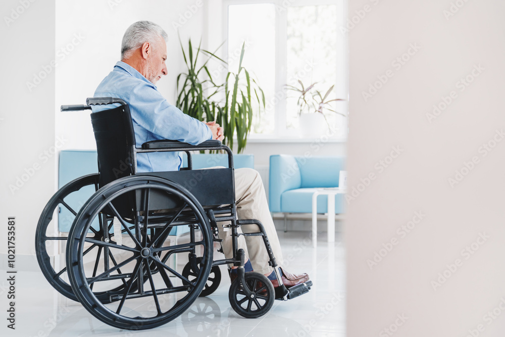 Sad elderly man sitting in wheelchair while looking out in window in retirement house Sad elderly man sitting in wheelchair while looking out in window in retirement house