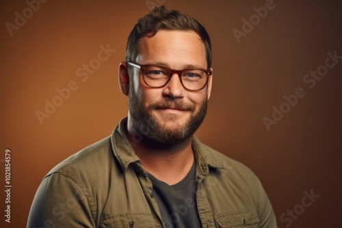 Portrait of a young man with a beard and glasses on a brown background