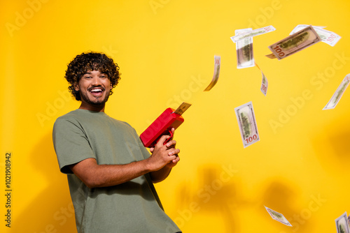 Photo of overjoyed guy with wavy hair dressed khaki t-shirt throwing fluttering dollars with gun isolated on yellow color background photo