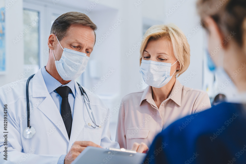 Doctor with patient and female receptionist working in medical protective masks in clinic lobby. Epidemic prevention concept Doctor with patient and female receptionist working in medical protective masks in clinic lobby. Epidemic prevention concept